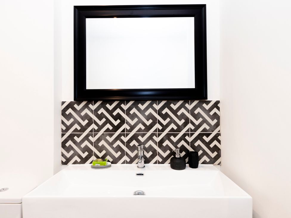 A bathroom sink with a faucet a black framed mirror and patterned tiles at Bishops Retreat in Ventnor