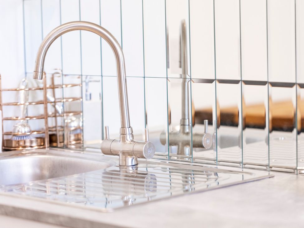 A kitchen sink with a chrome faucet and mirrored backsplash at Bishops Retreat in Ventnor