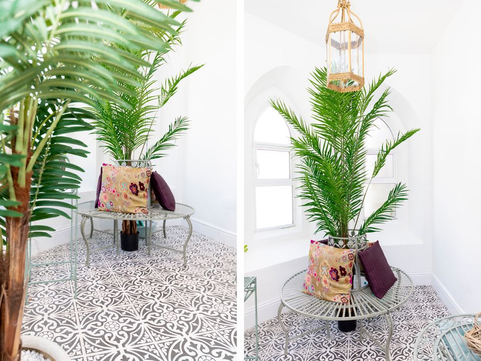 A corner seating area with a round metal bench around a potted plant with cushions and patterned floor tiles at Bishops Retreat in Ventnor