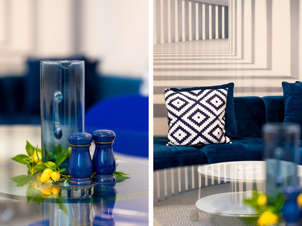 A living room with blue salt and pepper shakers on a glass table and a blue sofa with a patterned cushion at Bishops Retreat in Ventnor