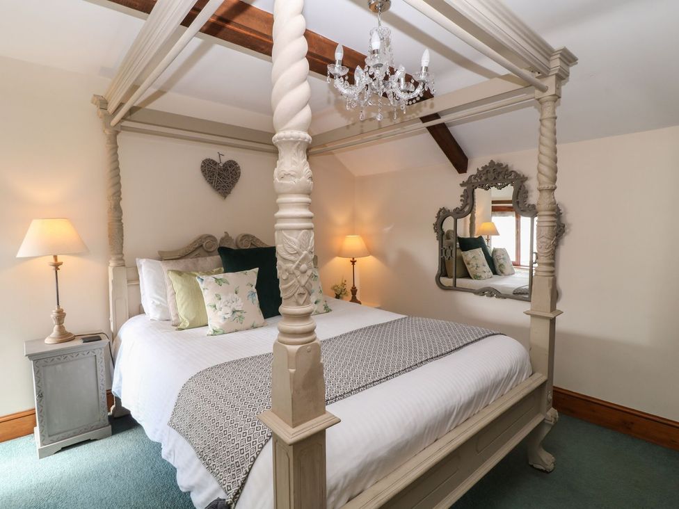 A bedroom with a four poster bed floral cushions bedside tables with lamps and a decorative mirror at Hazel Barn in North Molton