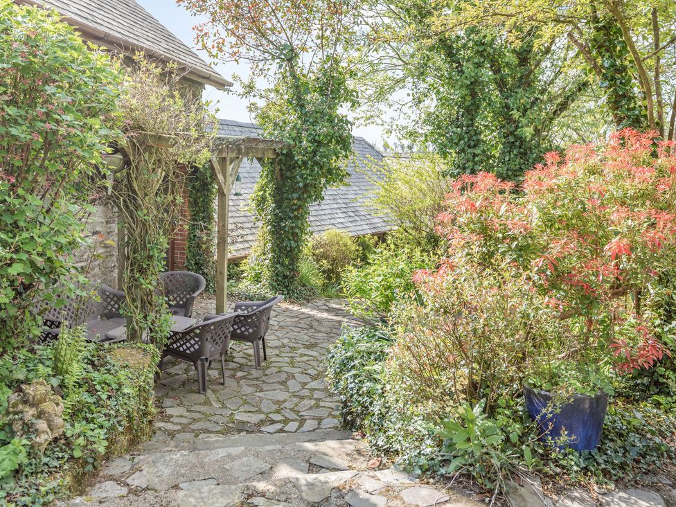 A stone patio with garden chairs and a table surrounded by plants and trees at Hazel Barn in North Molton