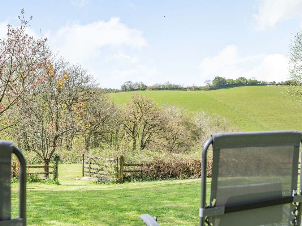 A grassy yard with two outdoor chairs facing a wooden gate and trees at Hazel Barn in North Molton