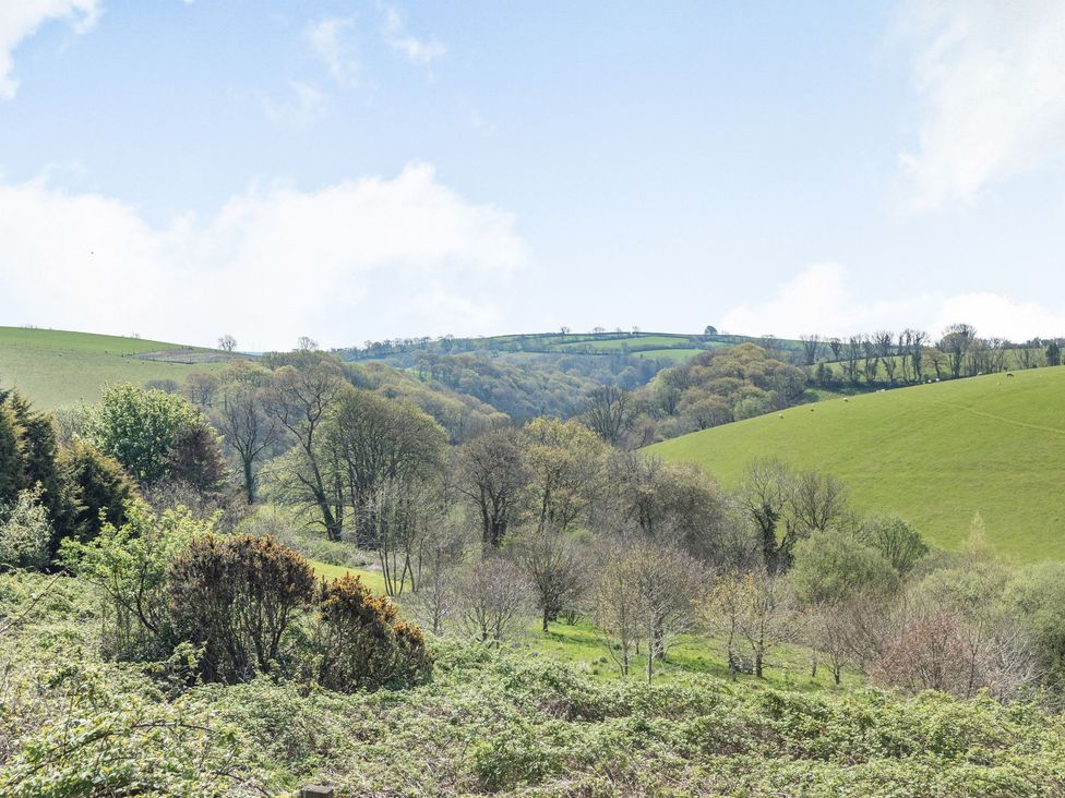 A landscape of rolling green hills with scattered trees under a partly cloudy sky at Hazel Barn in North Molton