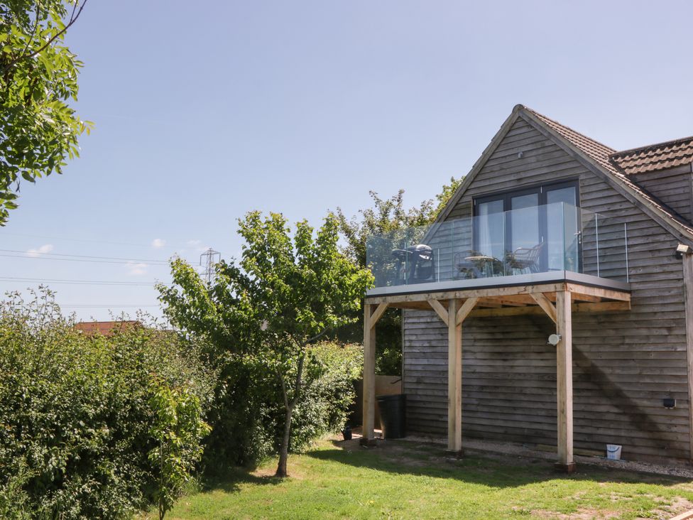 A wooden house with a glass balcony and outdoor furniture surrounded by trees and grass at Little Knaplock in Fiddington near Combwich Somerset