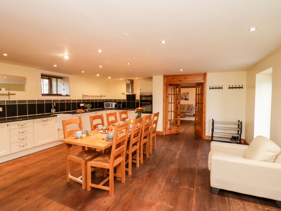 A kitchen and dining area with wooden table and chairs a cream sofa wooden floor and black tiled backsplash at The Old Dairy Ellerby in Runswick Bay
