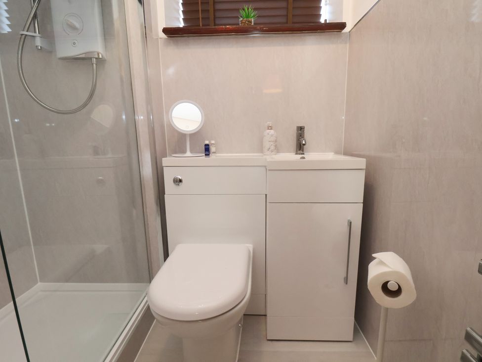 A bathroom with a toilet, sink, shower, small mirror, and toiletries at The Old Dairy, Ellerby in Runswick Bay