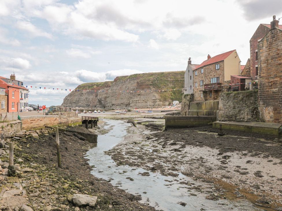 A coastal village with stone houses near a river with boats and cliffs in the background at The Barn in Staithes