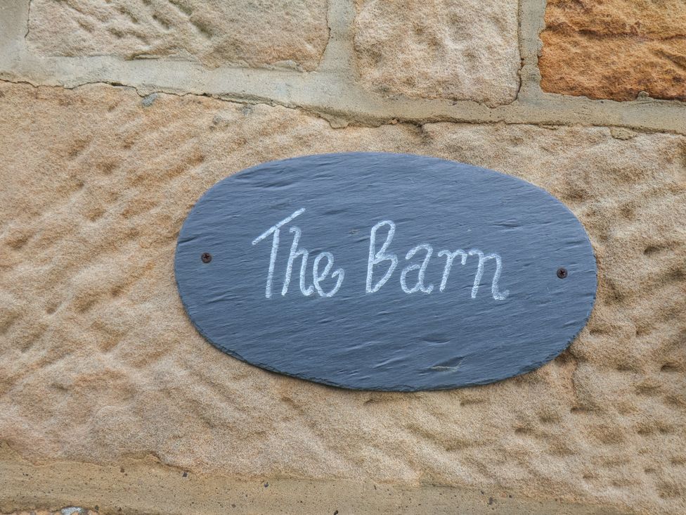 A black oval sign with The Barn written on it attached to a stone wall at The Barn in Staithes