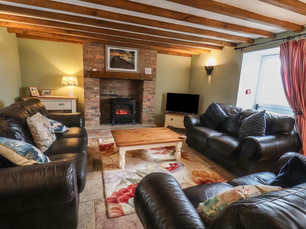 A living room with leather sofas a wooden coffee table a TV and a fireplace at The Barn in Staithes