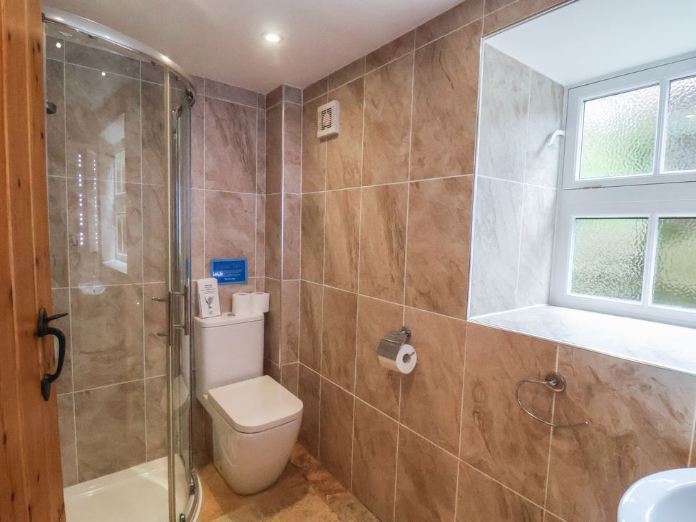 A bathroom with a shower, toilet, and a window at The Barn in Staithes