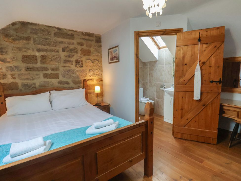 A bedroom with a wooden bed frame stone wall and an open door leading to a bathroom at The Barn in Staithes