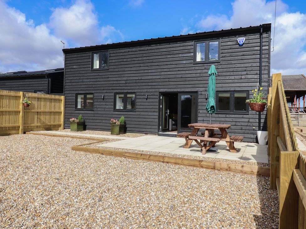 A black wooden house with gravel and a patio area with a wooden picnic table and green umbrella at The Old Dairy in Adisham near Wingham