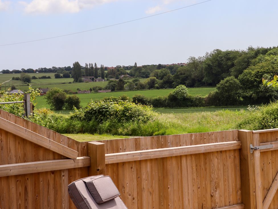 A wooden fenced garden with a cushioned chair overlooking green fields and trees at The Old Dairy in Adisham near Wingham