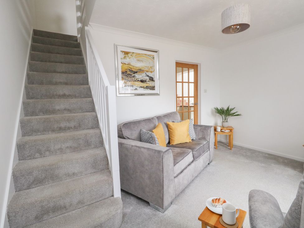 A living room with a grey sofa and yellow pillows next to a staircase and wooden side tables at Sandpiper in Weymouth
