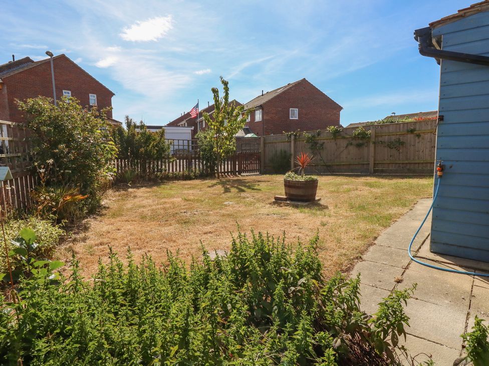 A backyard with a patchy lawn plants and a potted plant by a blue shed Sandpiper Weymouth