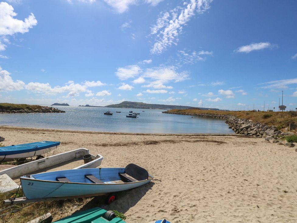 A sandy beach with small boats on the shore and more boats in the water at Sandpiper in Weymouth