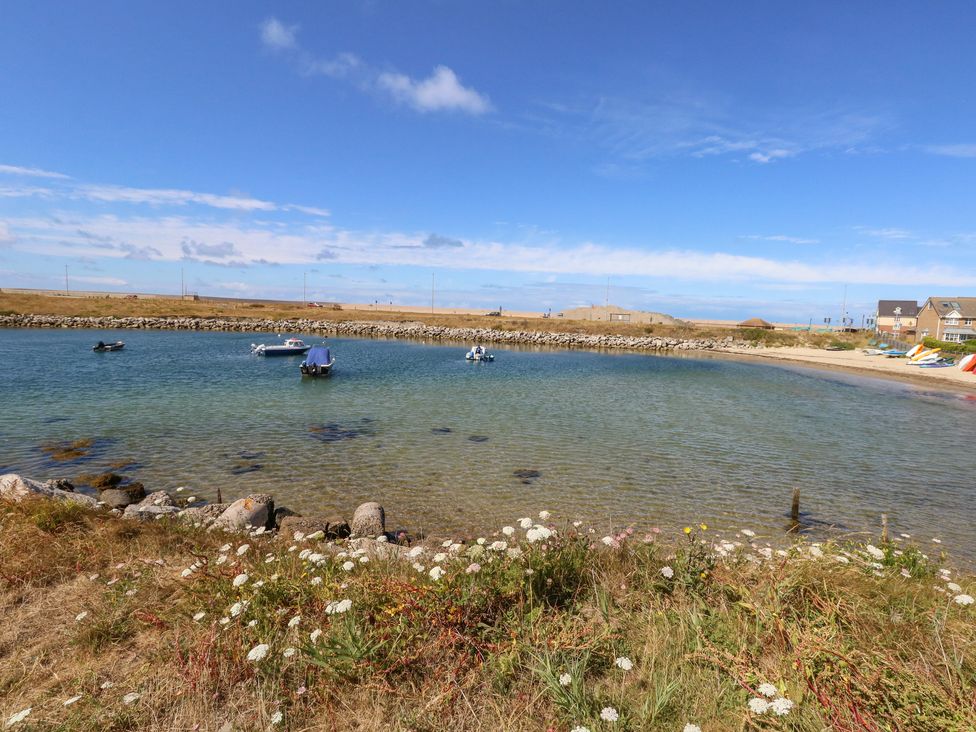 A small bay with several boats on clear water and wildflowers on the shore at Sandpiper in Weymouth