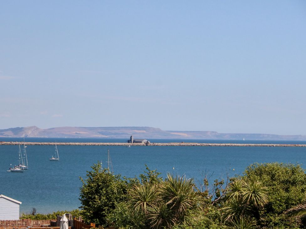 A coastal view with sailboats on water and a breakwater with buildings in the distance at Sandpiper in Weymouth