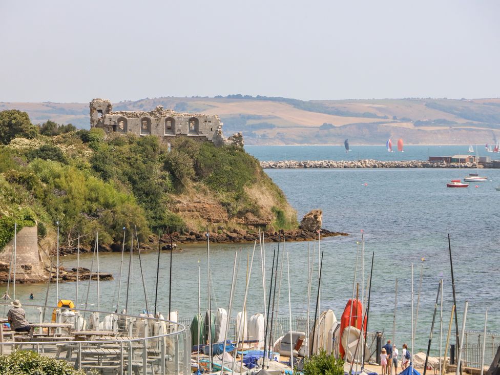 A coastal scene with sailboats docked near a ruined stone building on a hill at Sandpiper in Weymouth