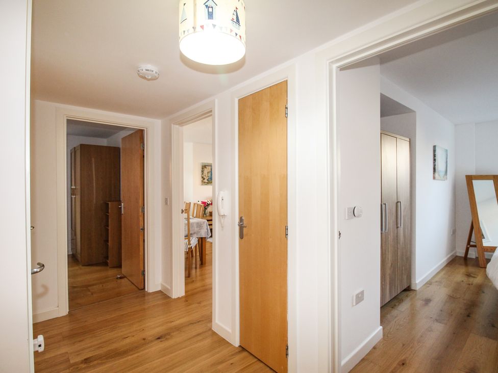 A hallway with wooden doors leading to different rooms with wooden floors and white walls at Broadleys in Swanage