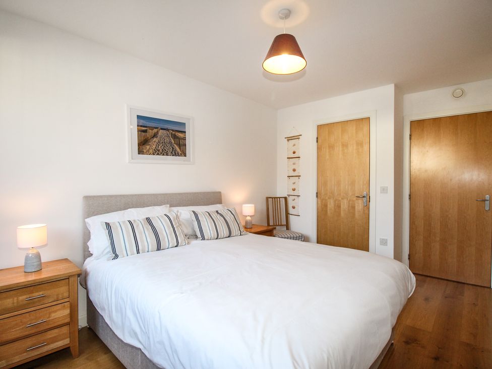 A bedroom with a double bed wooden bedside tables lamps and two wooden doors at Broadleys Swanage