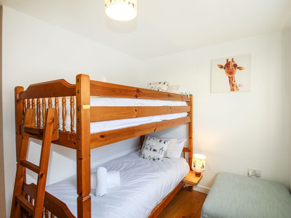A bedroom with wooden bunk beds pillows a bedside table with a lamp a green ottoman and a giraffe picture on the wall at Broadleys Swanage
