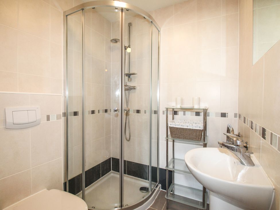 A bathroom with a glass shower enclosure a white sink a small metal shelf and a toilet at Broadleys Swanage