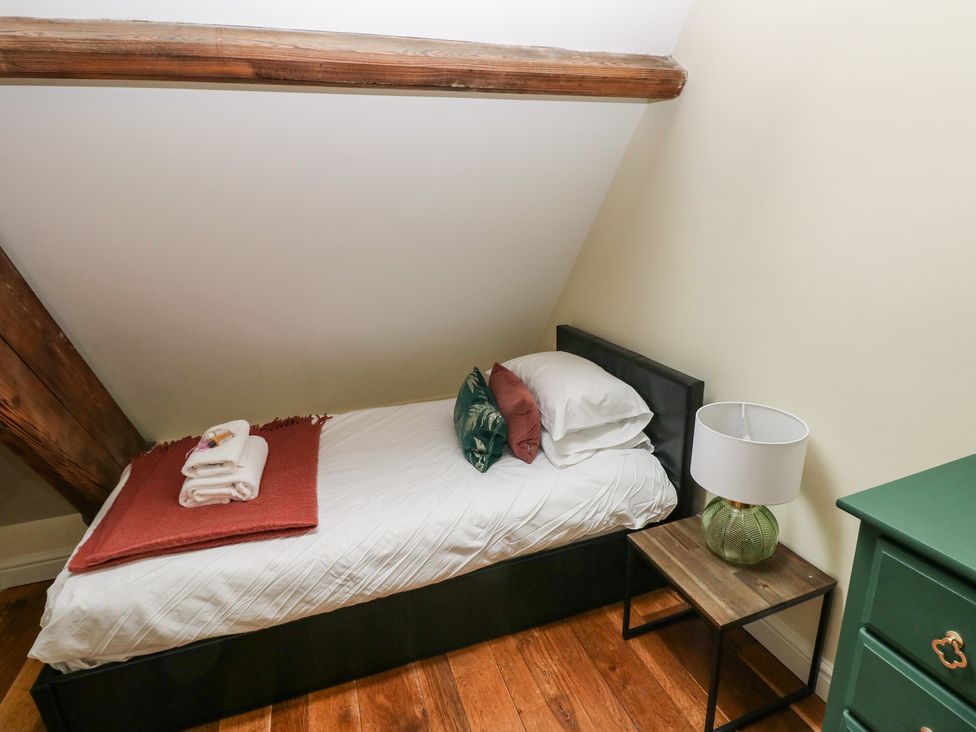 A small bedroom with a single bed white sheets and pillows a bedside table with a lamp and a green dresser at Oystermouth Chapel in Newton Swansea