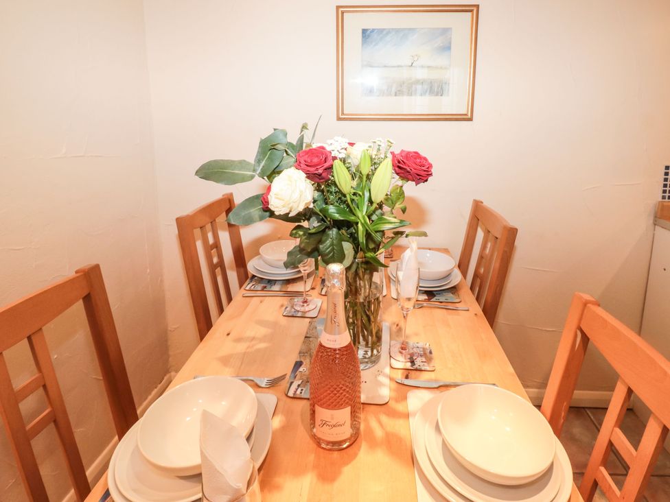 A dining table set with plates bowls cutlery glasses a bottle of rose wine and a flower arrangement at Bluebell Cottage in Marldon