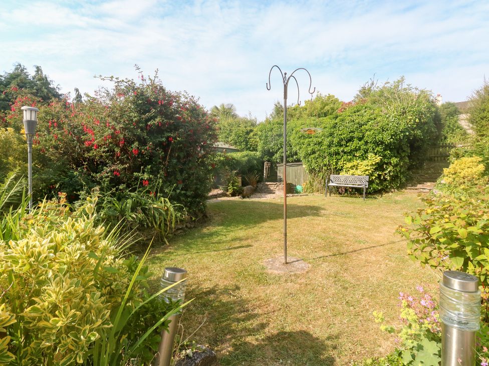 A garden with grass, plants, a bench, a bird feeder, and garden lights at Bluebell Cottage in Marldon