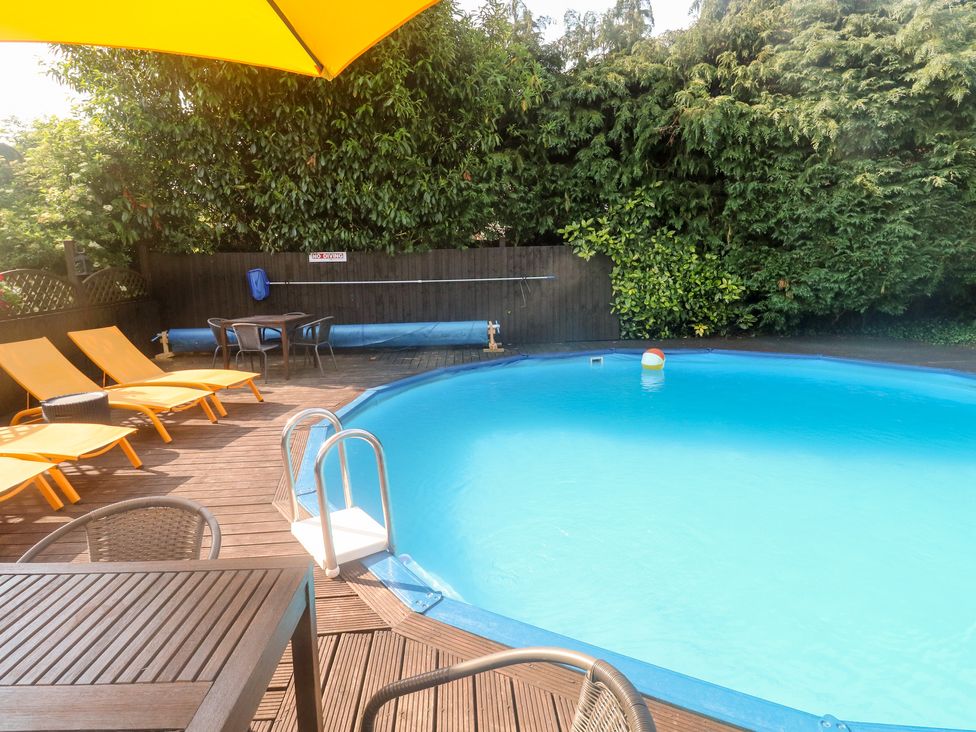 An outdoor pool area with a round swimming pool surrounded by wooden decking and lounge chairs at Bluebell Cottage in Marldon