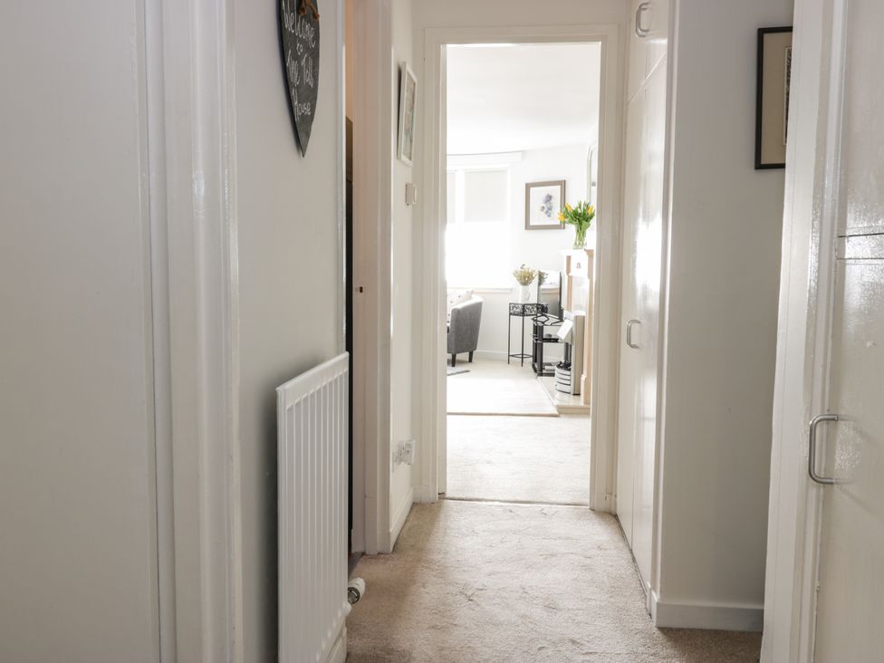 A hallway with white walls and beige carpet leading to a living room with chairs and a fireplace at The Toll House in Melrose