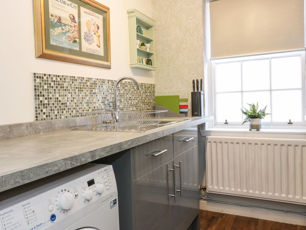 A kitchen counter with a sink, washing machine, knife block, cutting boards, and a window with a plant on the sill at The Toll House in Melrose