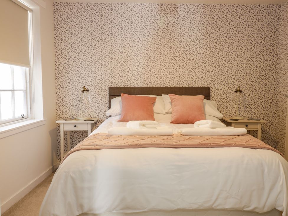 A bedroom with a bed with pink pillows and white linens beside two bedside tables with lamps at The Toll House in Melrose