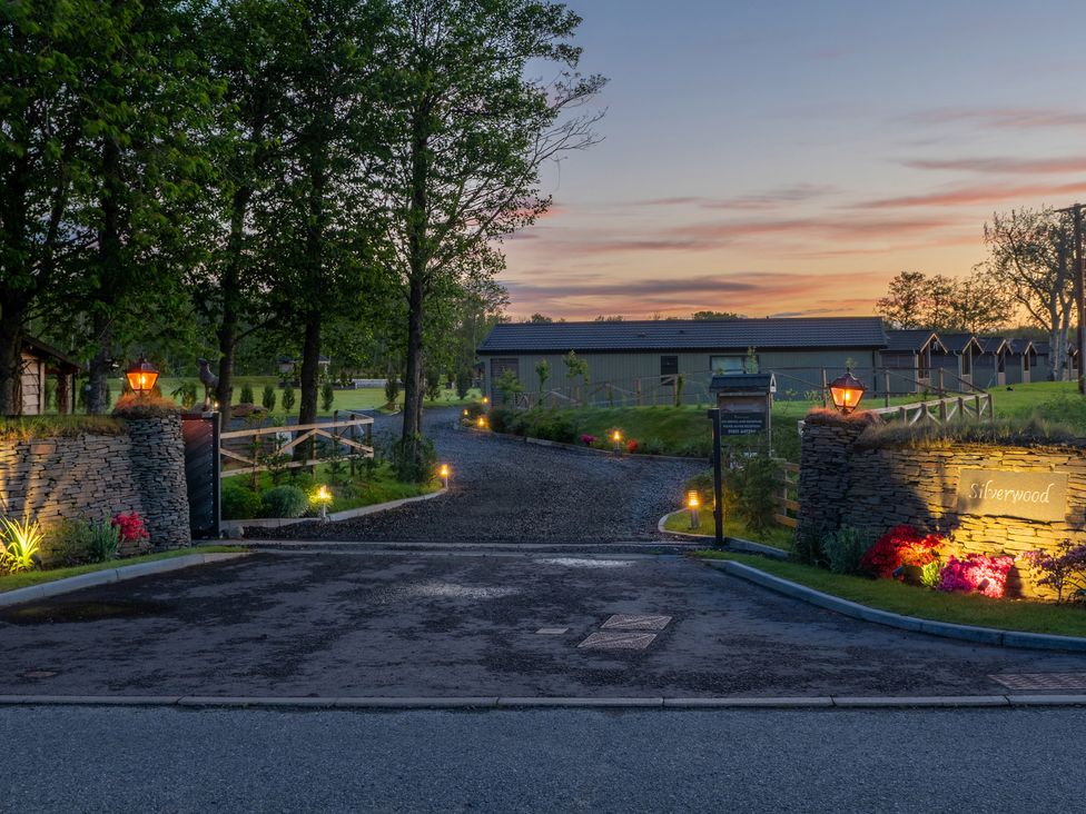 An illuminated entrance driveway with stone walls and lanterns leading to a building and fenced grassy area at Lodge 7 - The Earn in Errol