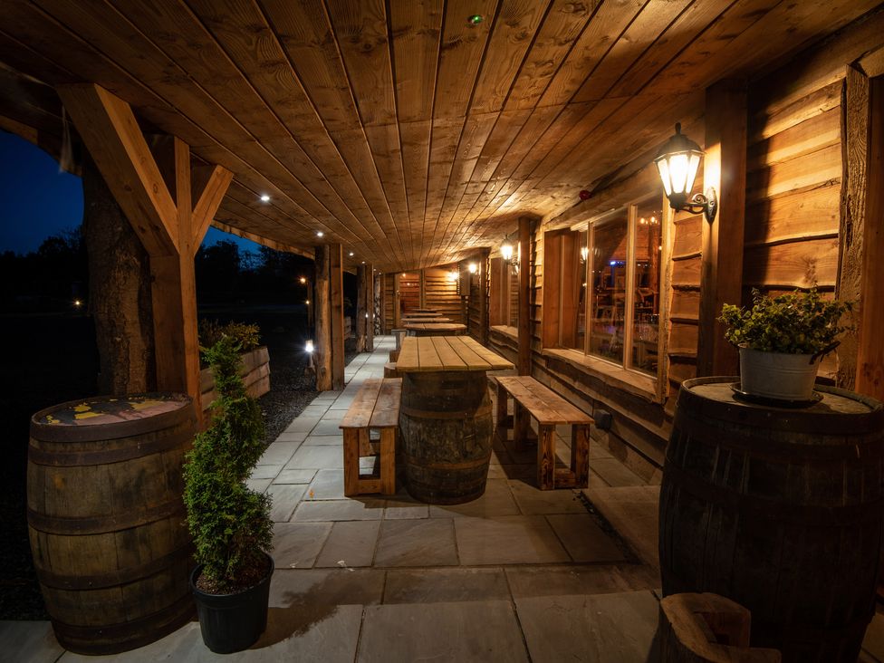 A covered outdoor seating area with wooden tables and benches on stone paving at Lodge 7 - The Earn in Errol