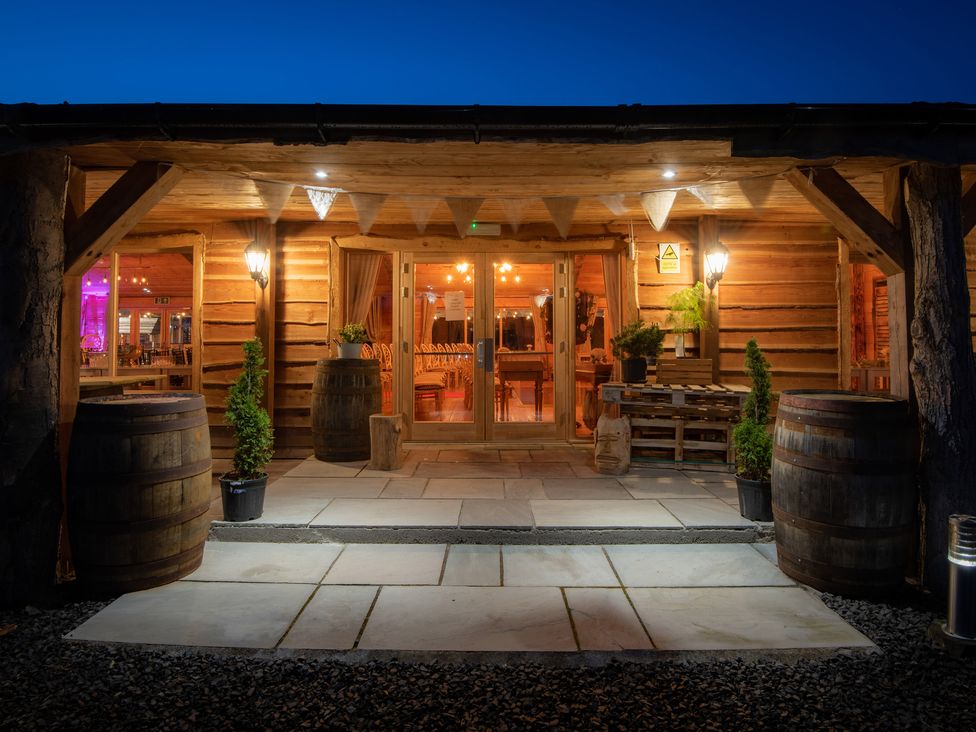 An entrance to a wooden lodge with barrels and potted plants on a stone patio at Lodge 7 - The Earn in Errol