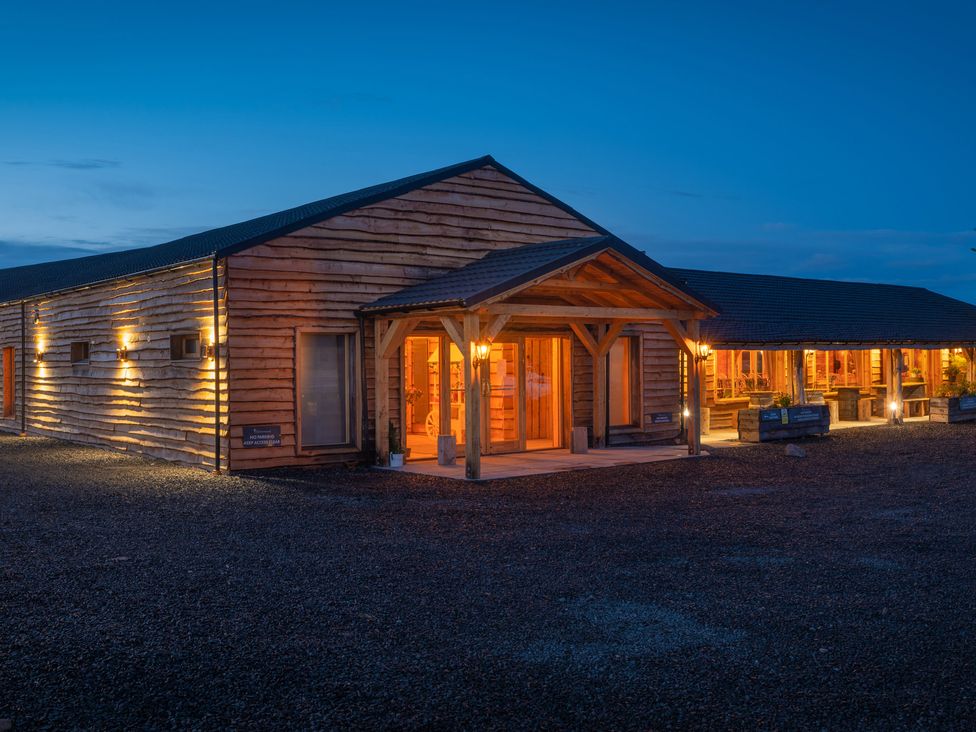 An exterior view of a wooden building with lit porch lights at dusk at Lodge 7 - The Earn in Errol