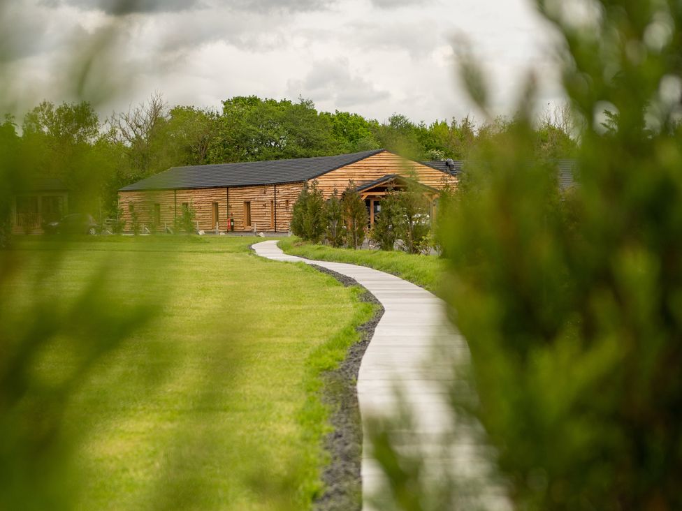 A winding paved path leading to a wooden building surrounded by grass and trees at Lodge 7 - The Earn in Errol