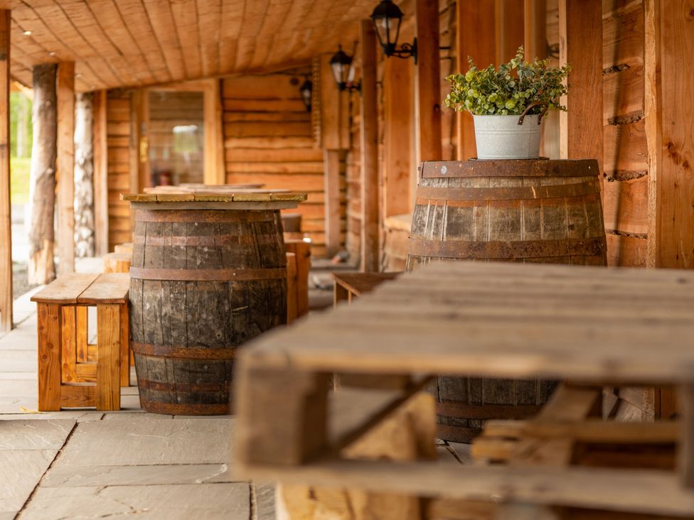 A wooden outdoor seating area with barrels used as tables and wooden benches at Lodge 7 - The Earn in Errol