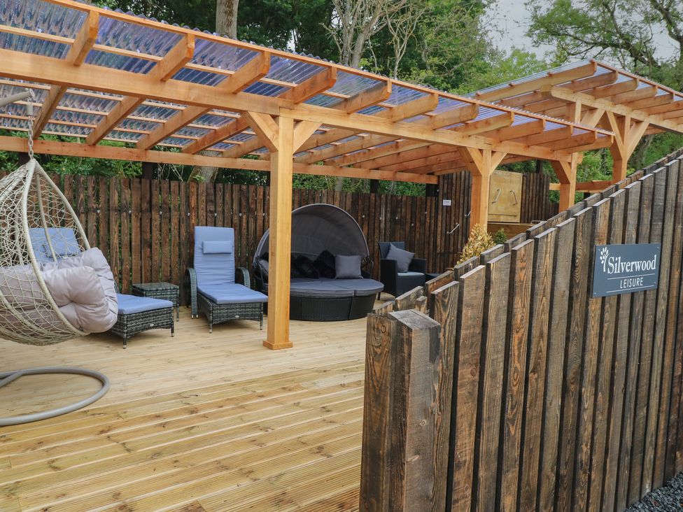 An outdoor wooden deck with lounge chairs hanging chair and a pergola at Lodge 7 - The Earn in Errol