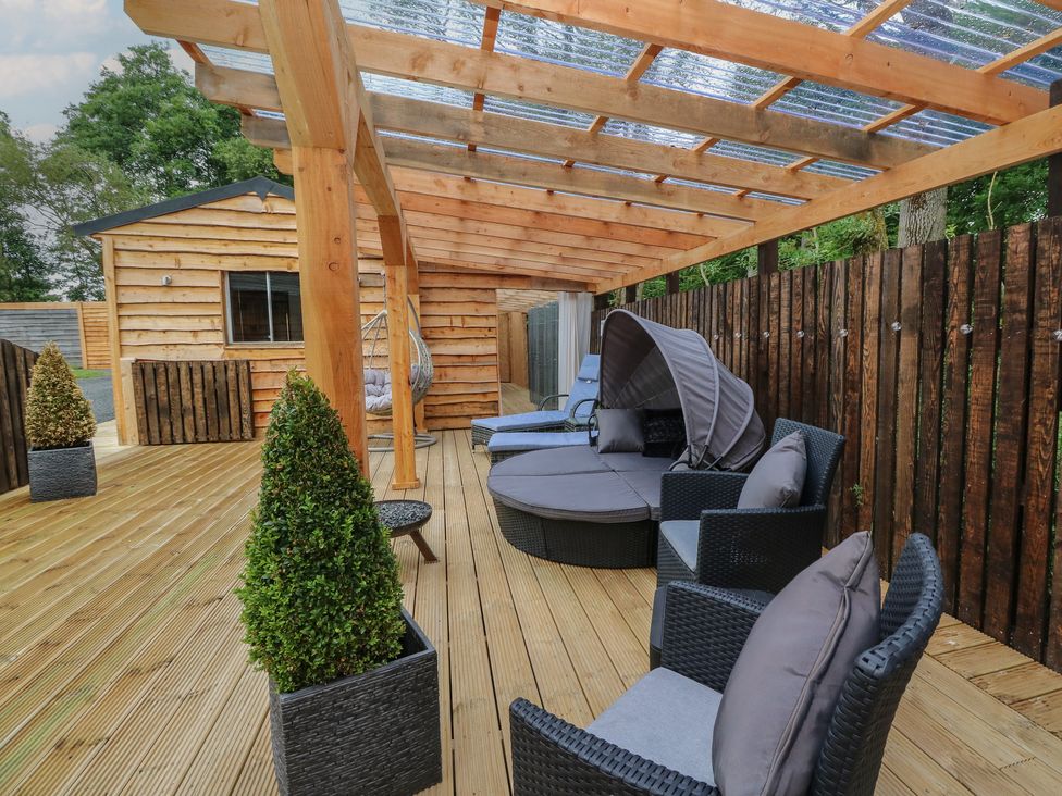 A covered wooden deck with outdoor seating furniture and potted plants at Lodge 7 - The Earn in Errol