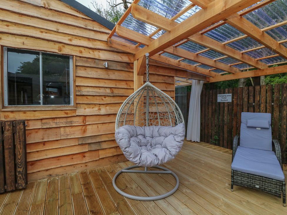 A wooden deck with a hanging chair and a lounge chair under a transparent roof at Lodge 7 - The Earn in Errol
