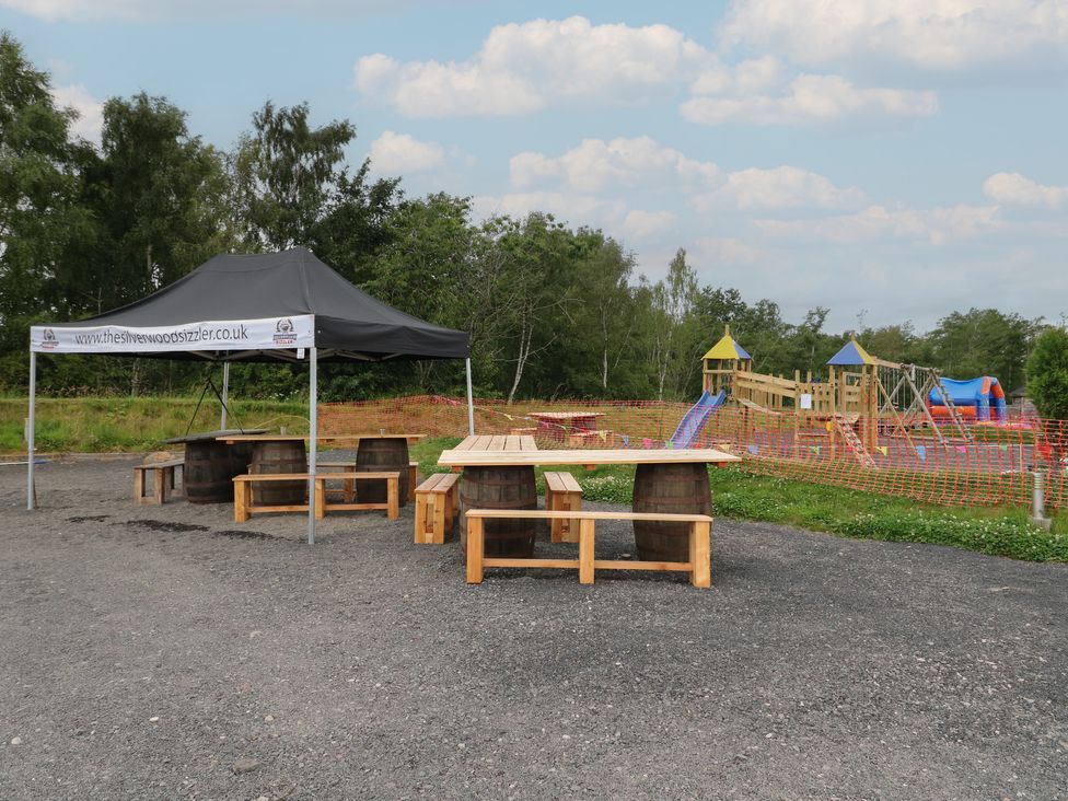 Outdoor seating area with wooden picnic tables and benches next to a playground at Lodge 7 - The Earn in Errol