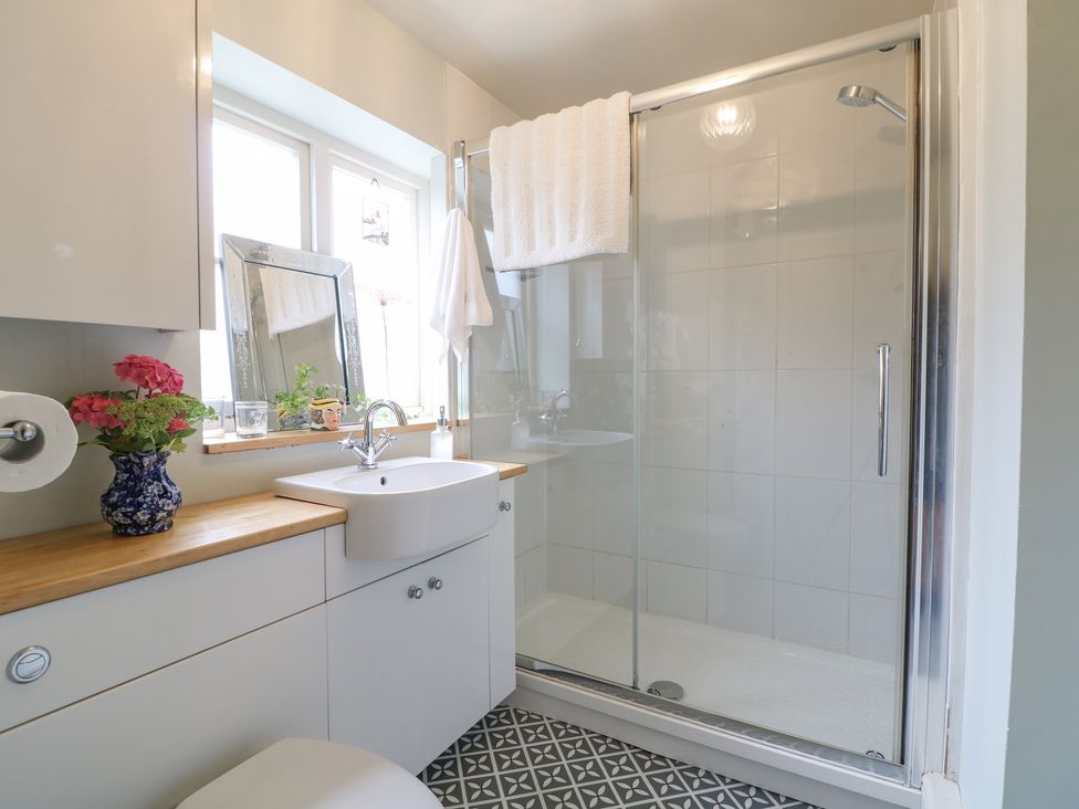 A bathroom with a sink countertop mirror and a glass-enclosed shower at The Snug No 35 West End in Minchinhampton