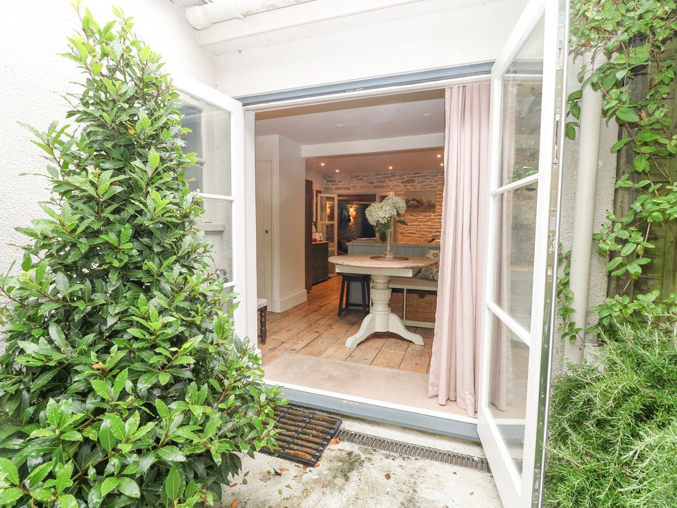 An open doorway from a garden into a room with a round table and flowers at The Snug No 35 West End in Minchinhampton