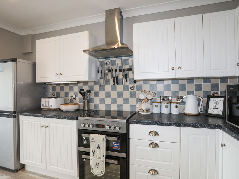 A kitchen with white cabinets stove and knives on a magnetic strip at 3 Tai Newydd in Llanfaelog near Rhosneigr