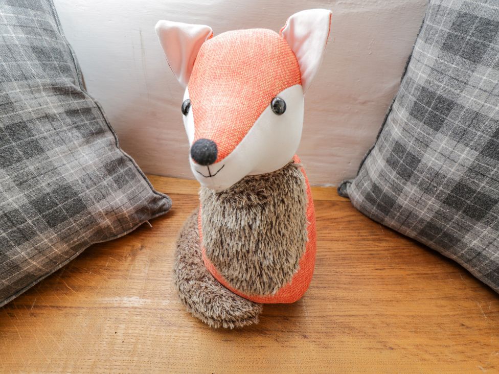 A stuffed fox toy placed on a wooden surface between two gray checkered cushions at Fox Den Cottage in Castle Combe