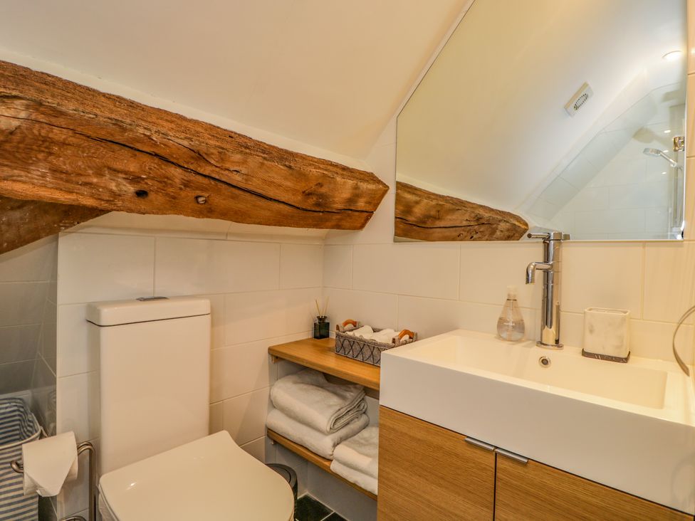 A bathroom with a toilet sink wooden shelves towels and a large mirror at Fox Den Cottage in Castle Combe